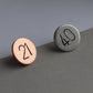 Two birthday badges, one is for a 21st birthday and the other for a 40th. the 21st birthday pin is copper and the 40th pin is silver.