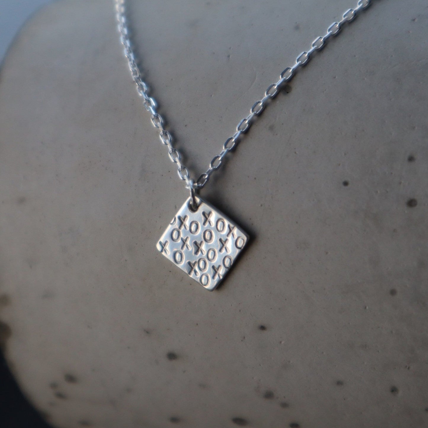 XOXO Pendant on a Sterling Silver Chain displayed on a cement background.