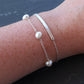 A Satellite Pearl Bracelet displayed with a skinny bar bracelet. Both are made rfom sterling silver.